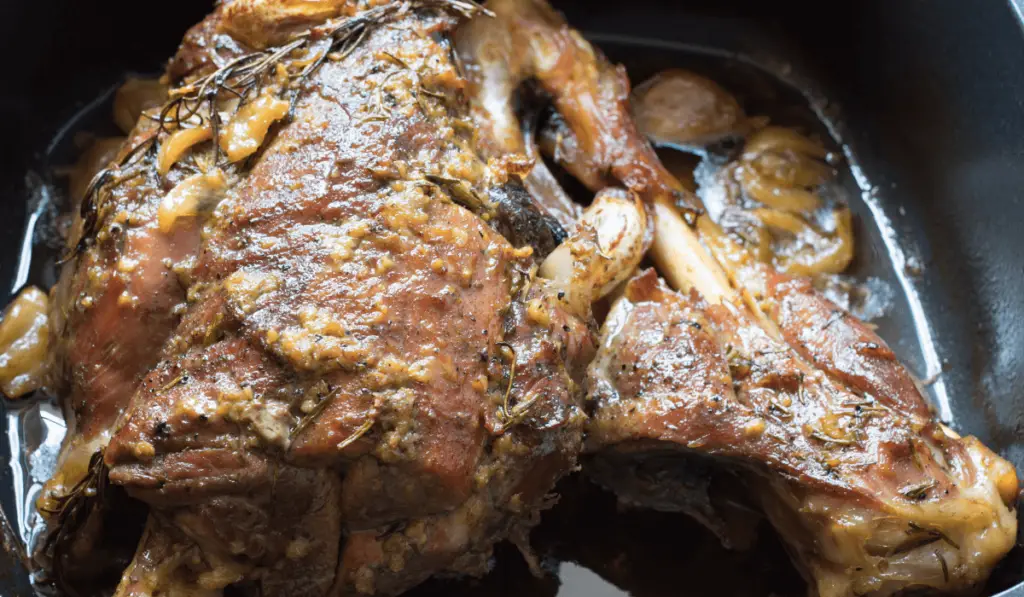 Oven-baked lamb leg steak on a serving platter garnished with rosemary and thyme.